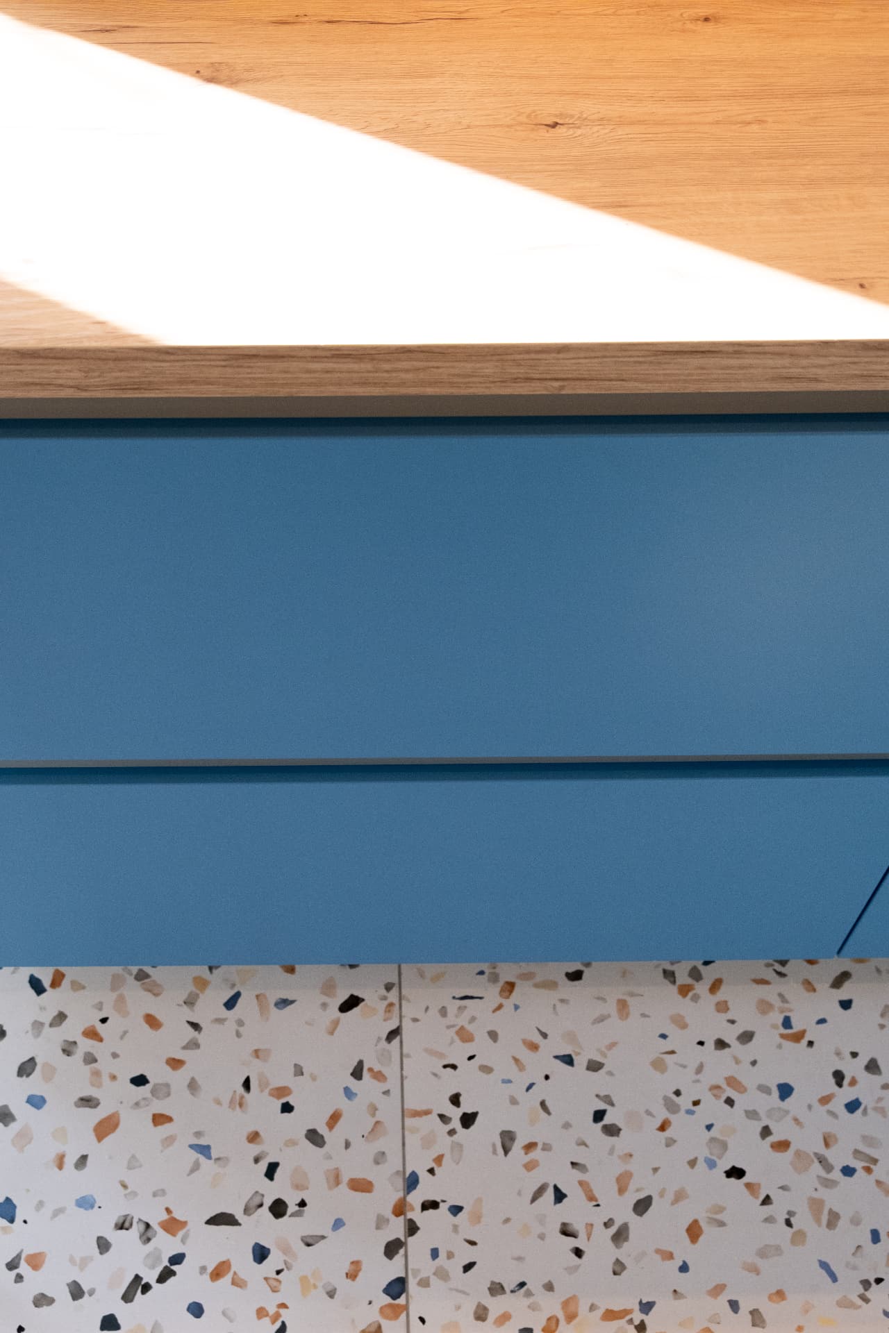 Oak worktop meeting deep blue drawer fronts above a terrazzo floor