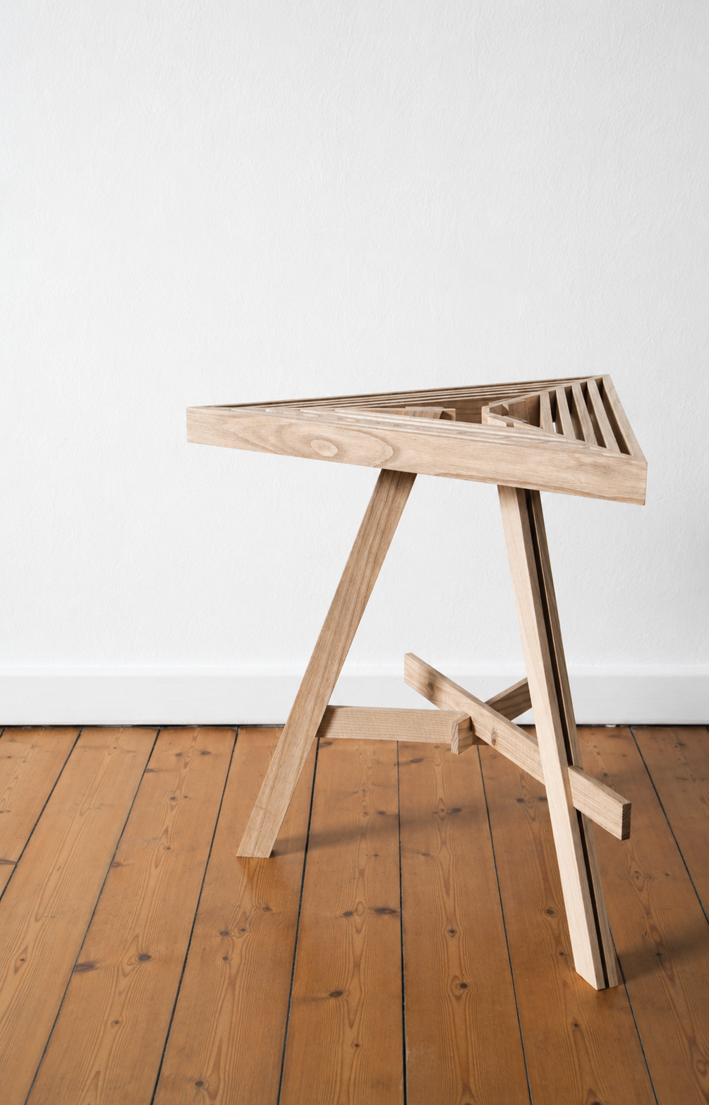 Ash stool with a slatted triangular seat and tripod frame on a wooden floor