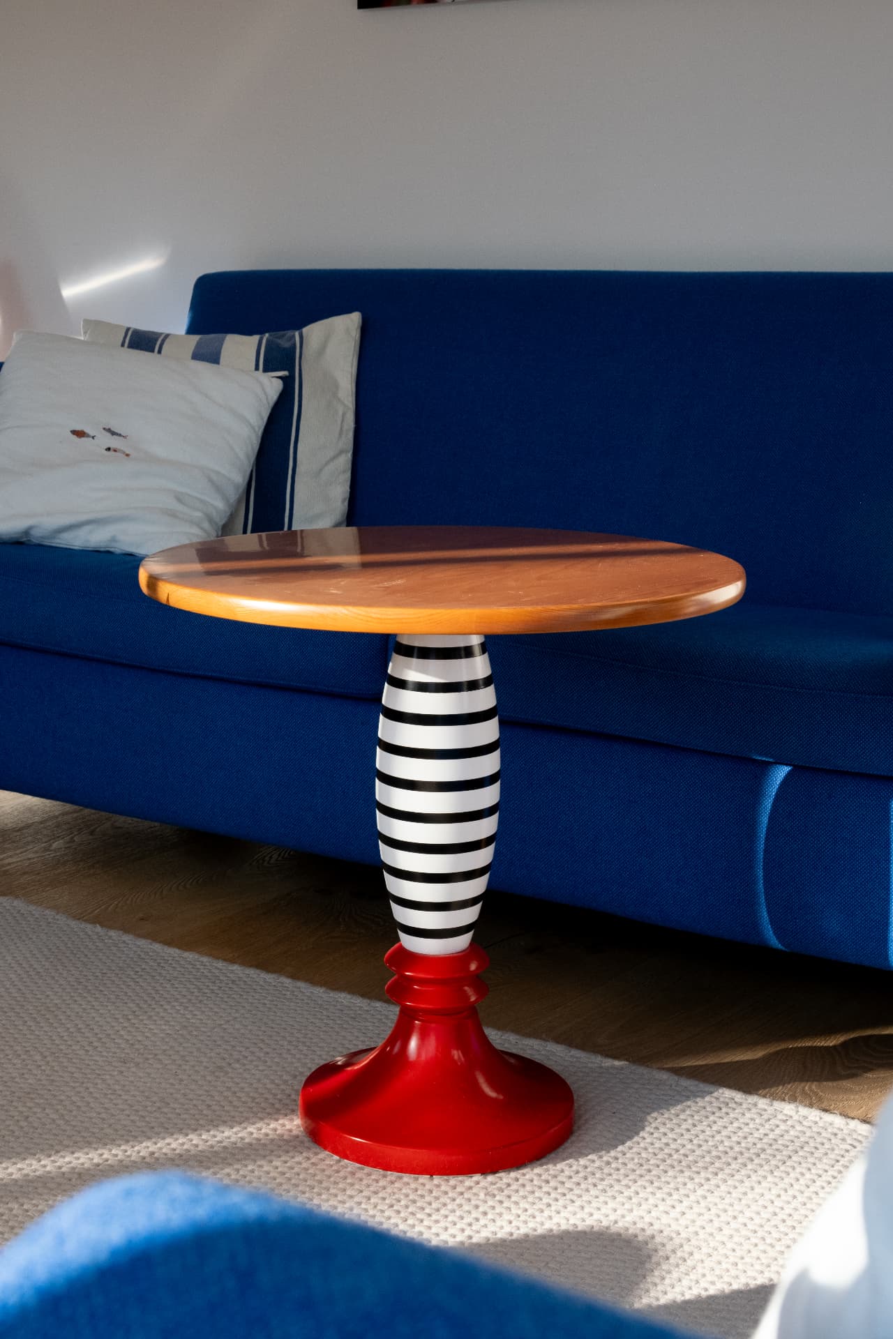 Blue sofa with a sculptural side table on a pale wool rug in daylight