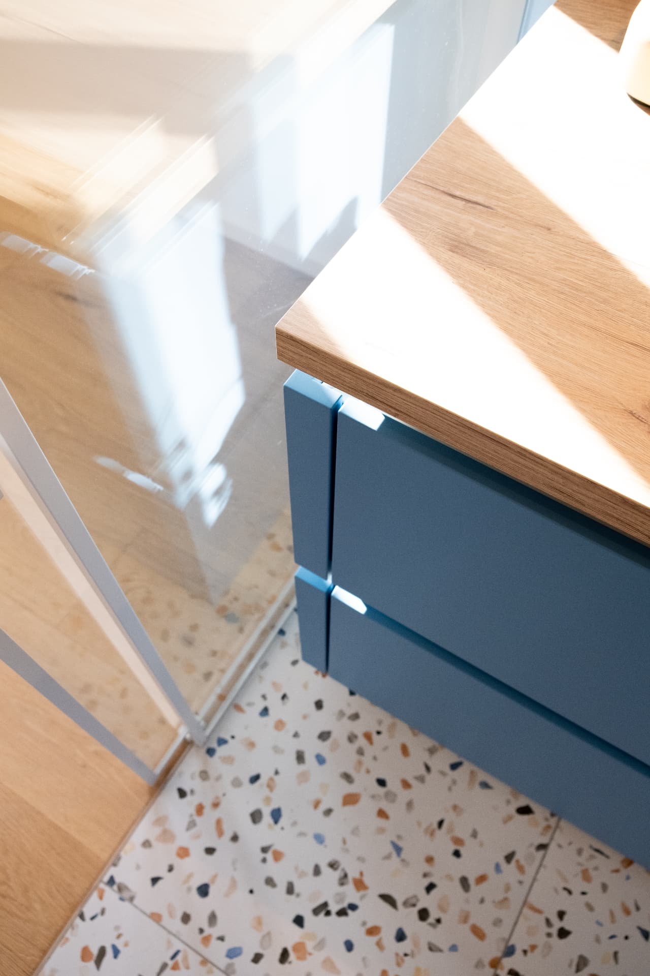 Oak worktop meeting blue cabinetry above a pale terrazzo floor